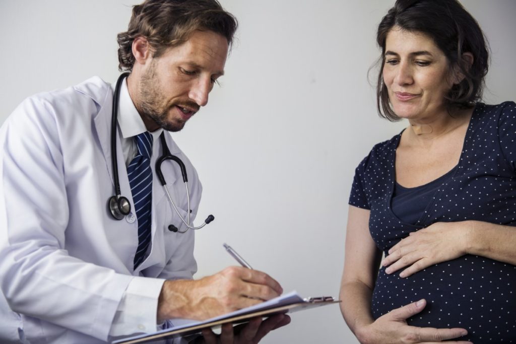 Imagem de médico examinando paciente grávida no período pré-natal.
