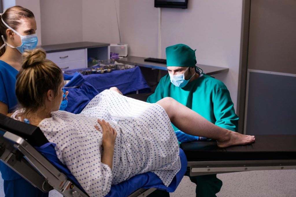 Imagem de mãe realizando parto com apoio de médico obstetra e enfermeira.
