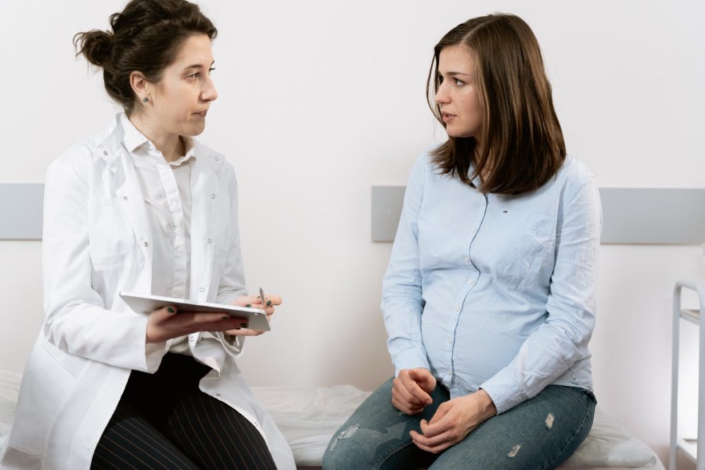 Imagem de médica e paciente grávida conversando, com a médica fazendo anotações de informação no período pré-natal.