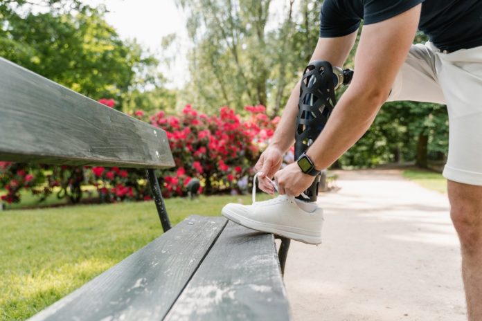 Imagem de jovem com perna prostética amarrando o tênis no banco de um parque, presente no texto do blog da Sami sobre o tema: Plano de saúde cobre próteses ou órteses?