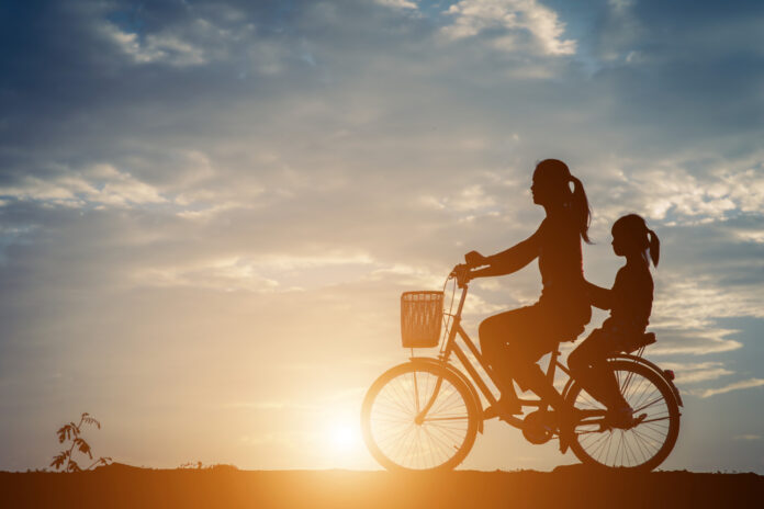 Imagem de mãe e filha fazendo passeio de bicicleta ao pôr do sol, presente no texto sobre o que são os determinantes sociais da saúde do blog da Sami