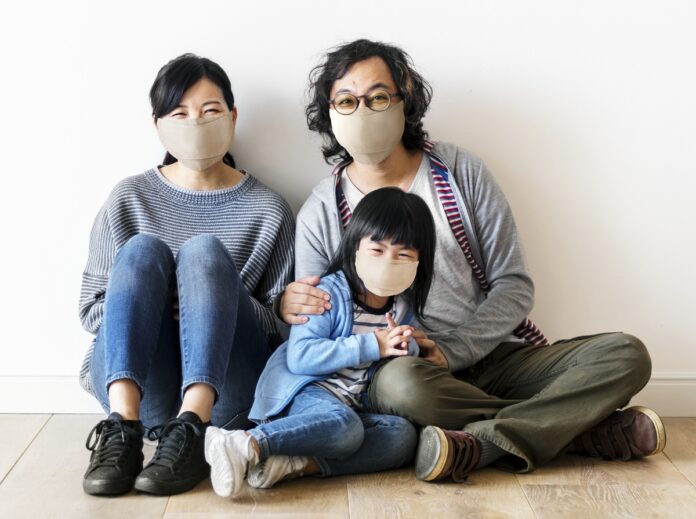 Imagem de família com pai, mãe e filha, de origem oriental, sentados no chão de máscara sorrindo, presente no texto do blog da Sami sobre plano de saúde custo benefício
