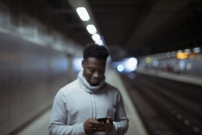 Imagem de jovem colaborador feliz mandando mensagem no metrô, presente no texto sobre flexibilidade no trabalho e como o RH pode promovê-la