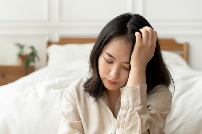 Mulher asiática sentada triste ao lado da cama